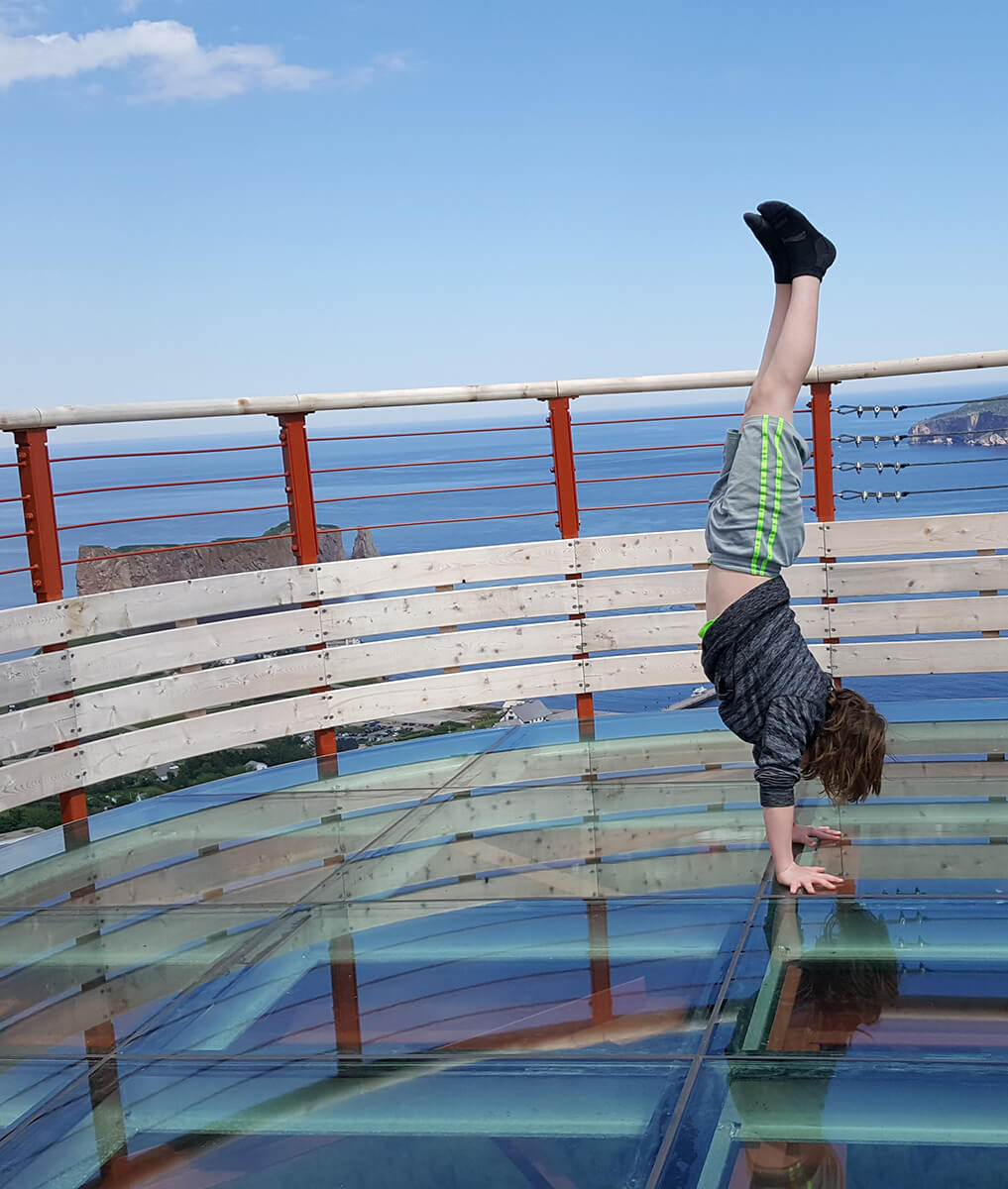 Un enfant fait se tient sur les mains sur la plateforme vitrée du Géoparc de Percé