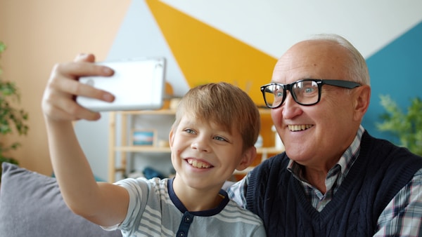 Joyful people old man and boy are taking selfie at home posing smiling using smartphone camera. Contemporary devices, photograph and happy family concept.
