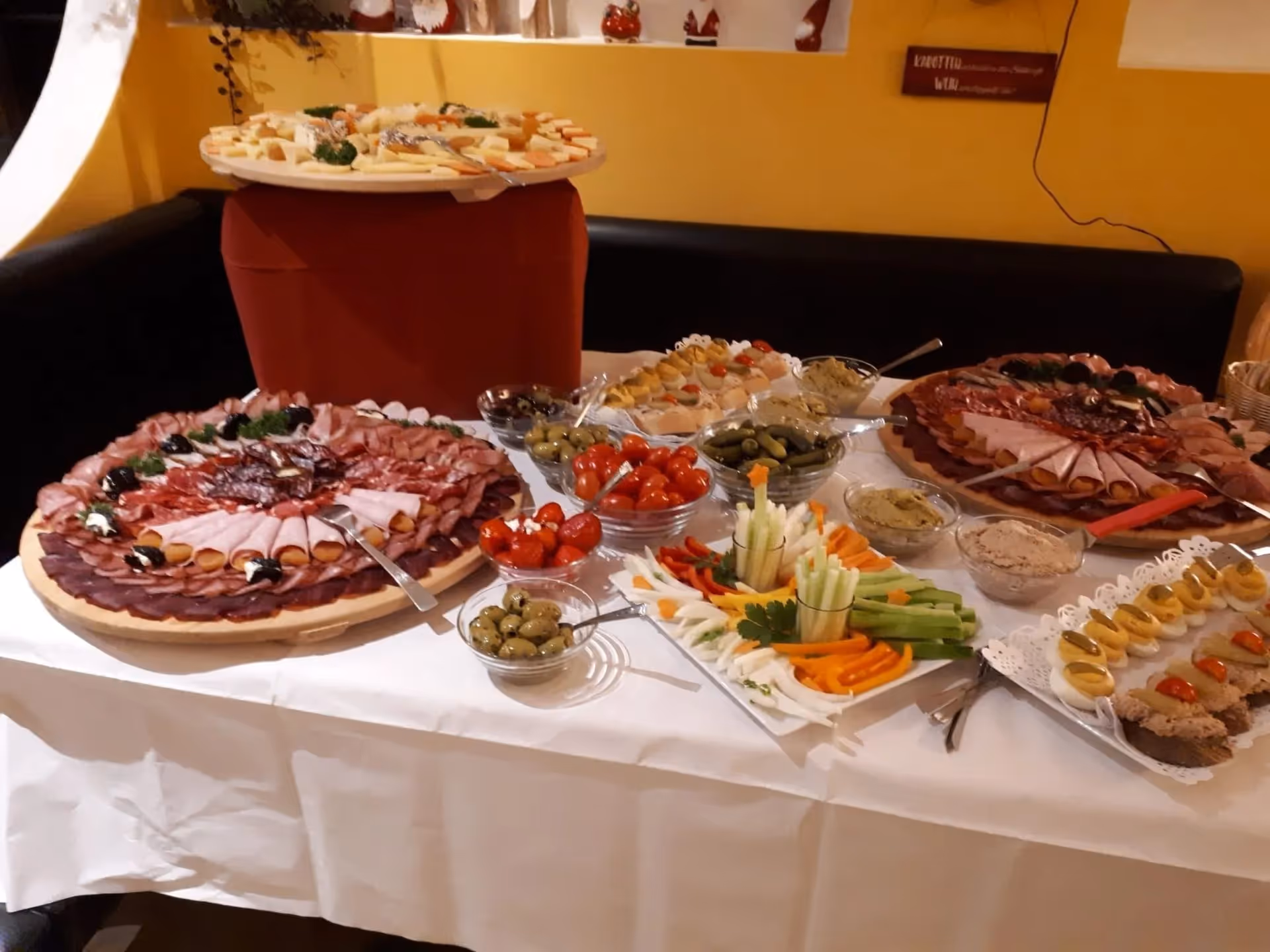 Buffet table with assorted cold cuts, cheeses, olives, cherry tomatoes, pickles, vegetable sticks, and spread appetizers.