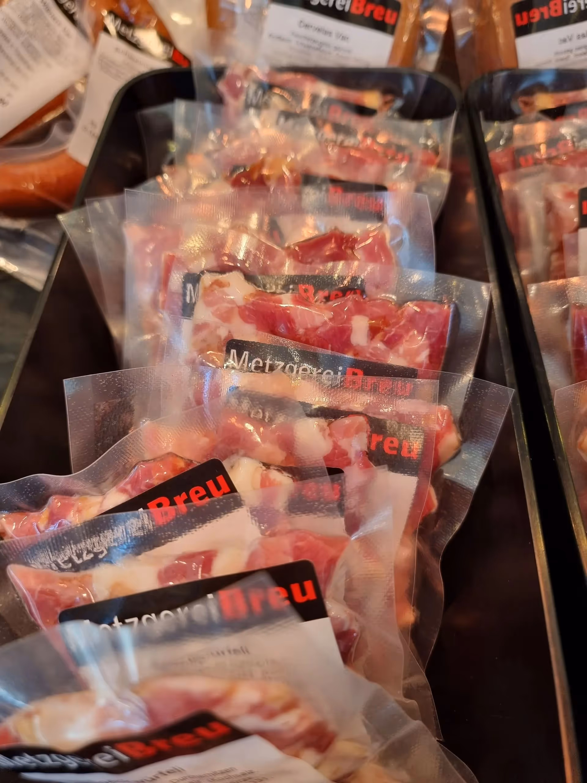 Vacuum-sealed packages of sliced cured meat displayed in rows on a dark tray.