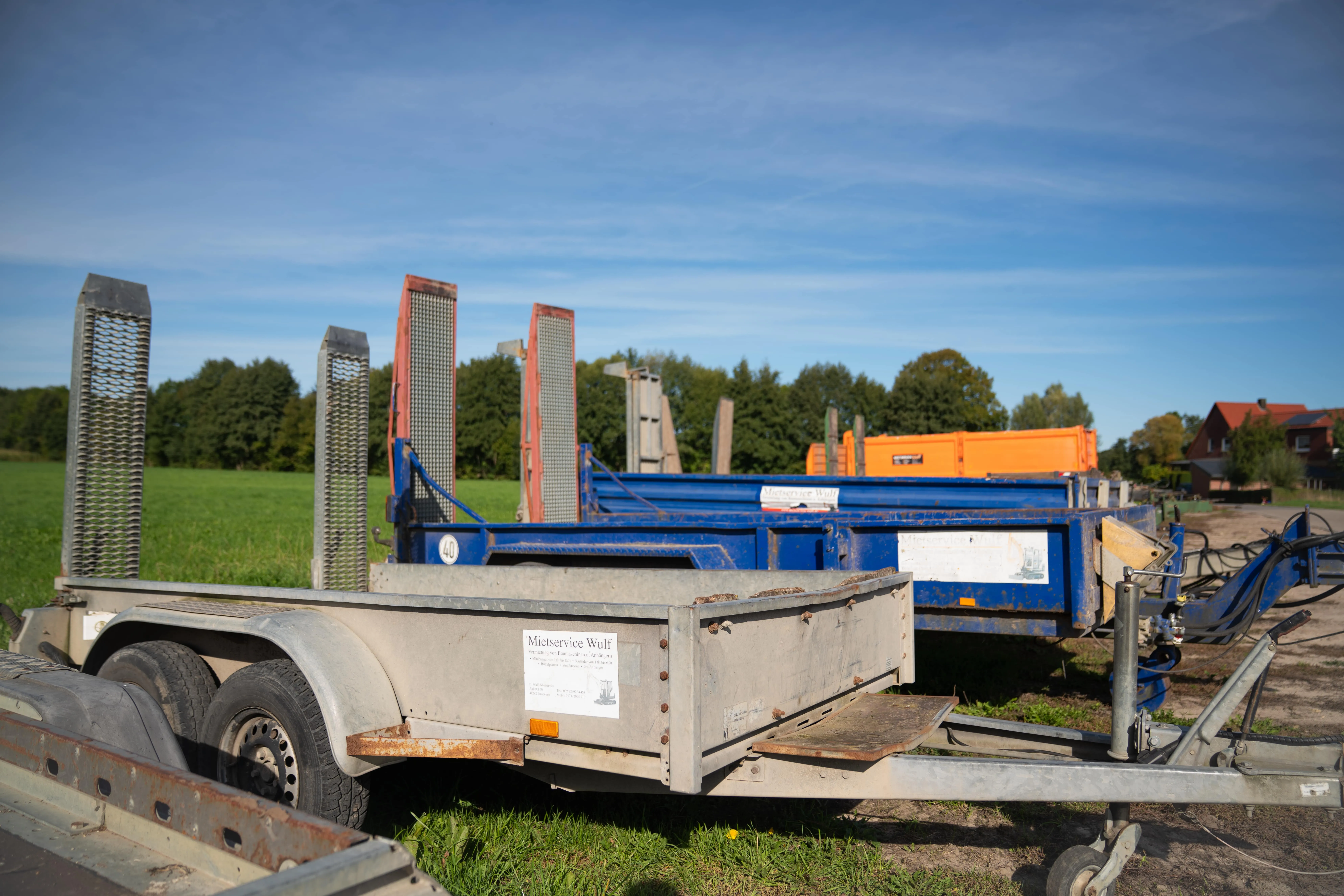 Mehrere Parkanhänger unterschiedlichen Typs, darunter blaue und graue, auf einem Feld unter blauem Himmel geparkt.