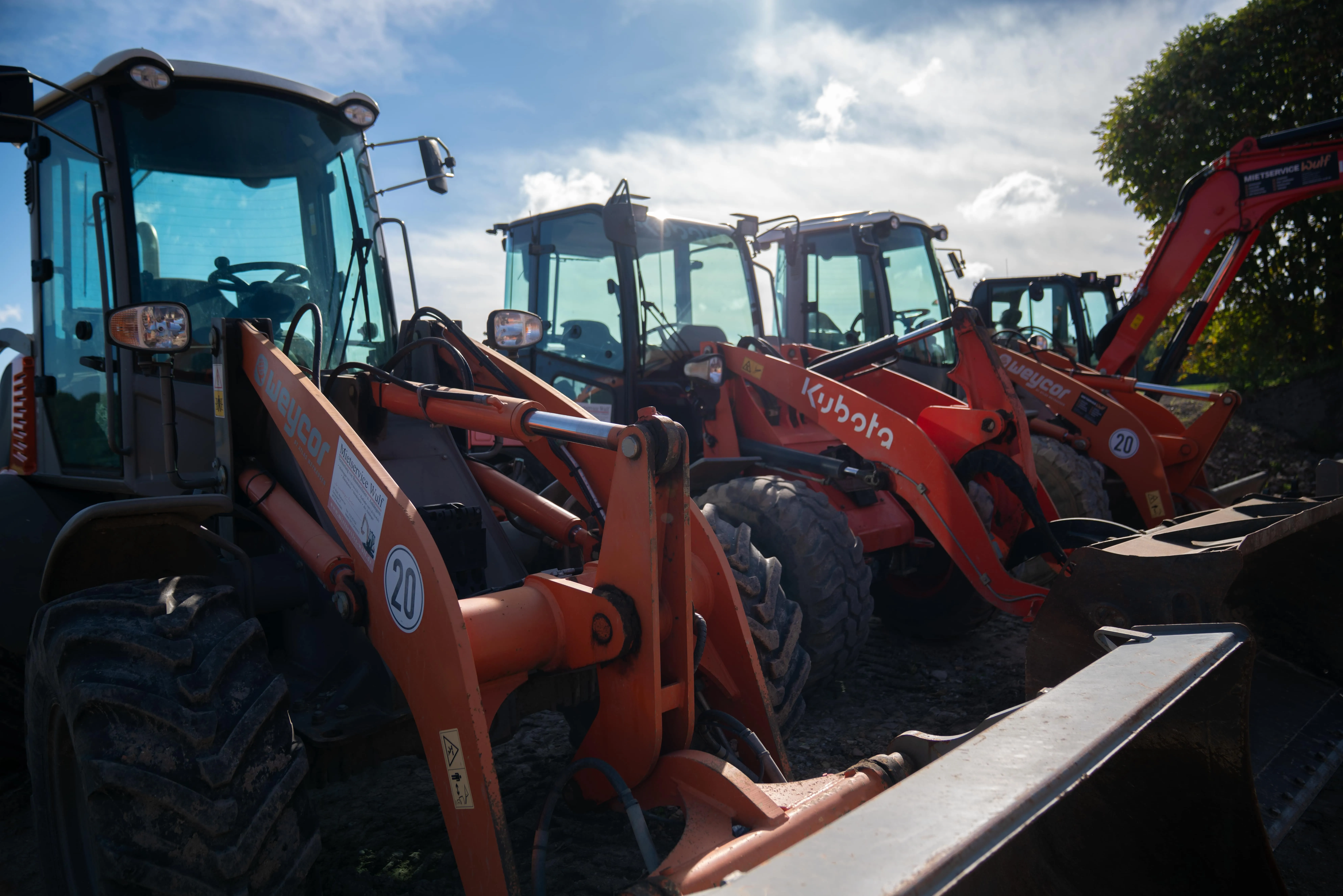 Vier geparkte orangene Radlader verschiedener Marken bei bewölktem Himmel.