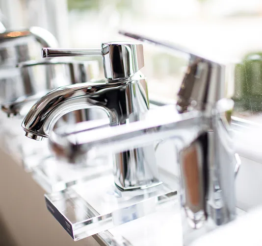 Mehrere glänzende verchromte Wasserhähne auf einer Ausstellungsvitrine mit unscharfem Hintergrund.