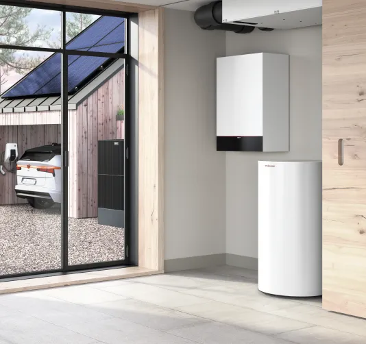 Moderne Heizungsanlage in einem hellen Raum mit Fenster, das eine Garage mit einem Elektroauto und Solarpaneelen zeigt.
