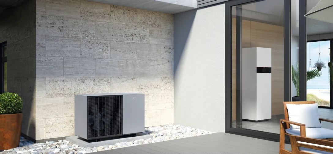 Moderne Wärmepumpe außen an einem Haus mit einer weißen Einheit im Innenraum, neben einer Terrasse mit Holzstuhl und Pflanzen.