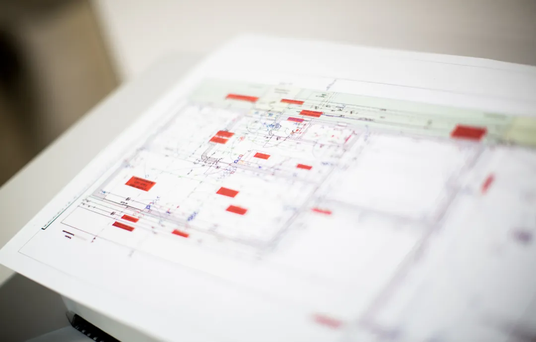 Architekturplan mit roten Markierungen auf einem weißen Tisch liegend.