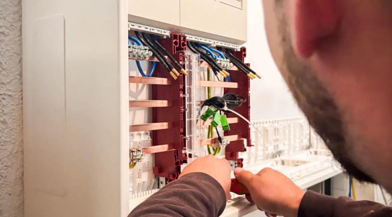 Elektriker arbeitet an einem offenen Verteilerkasten mit mehreren Kabeln und Leitungen.