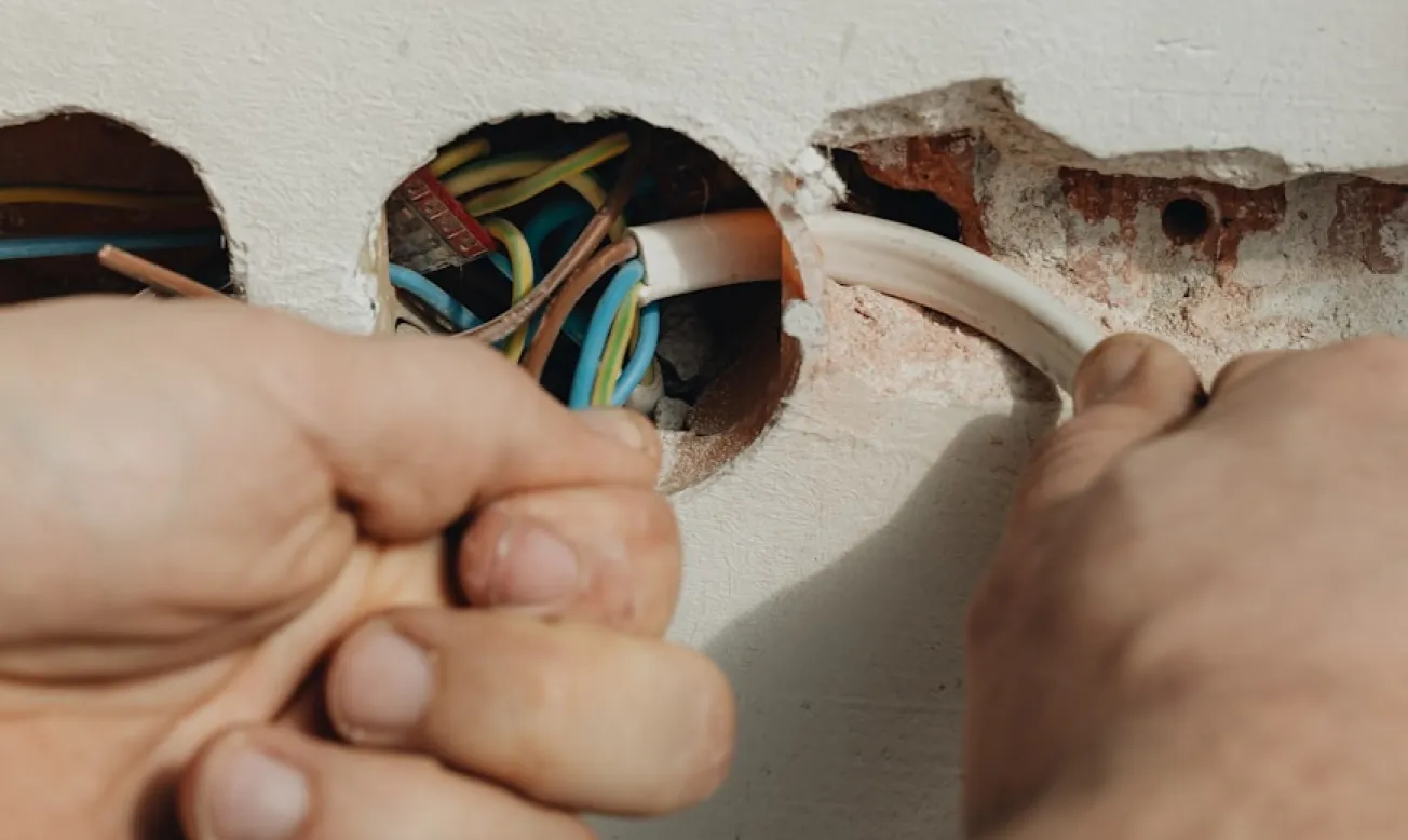 Hände eines Elektrikers, der Kabel in eine runde Bohrung in der Wand zieht und ordnet.