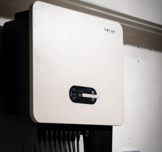 Weißes Wandgerät mit kleinem Display und mehreren Kabeln unten, montiert an einer Wand.