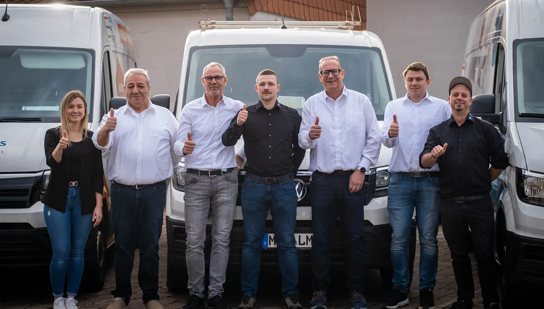 Sieben Personen stehen vor drei weißen Lieferwagen und zeigen jeweils Daumen nach oben.