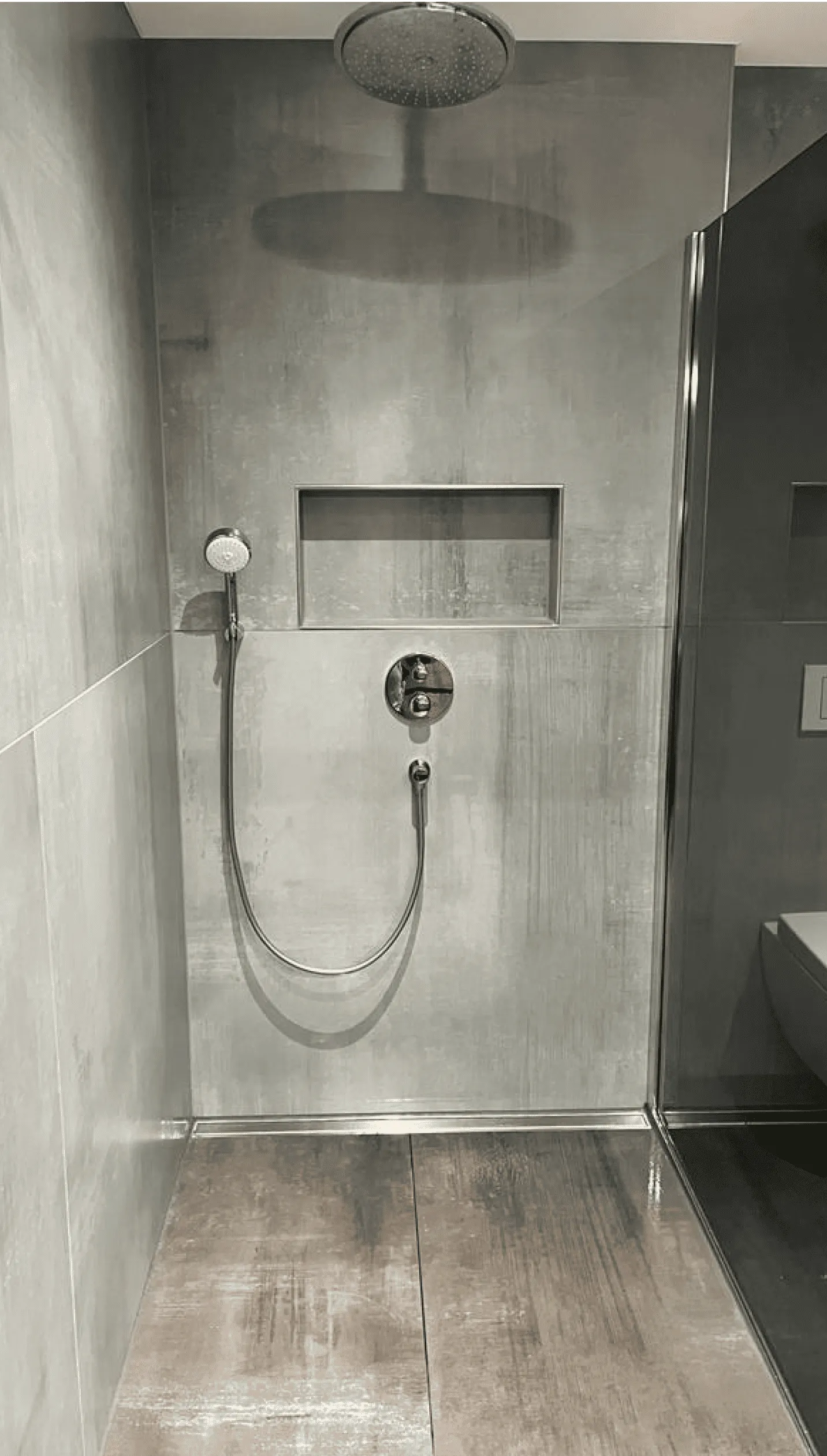 Moderne Walk-In-Dusche mit Regendusche, Handbrause und eingebautem Wandfach in grauer Fliesenoptik.