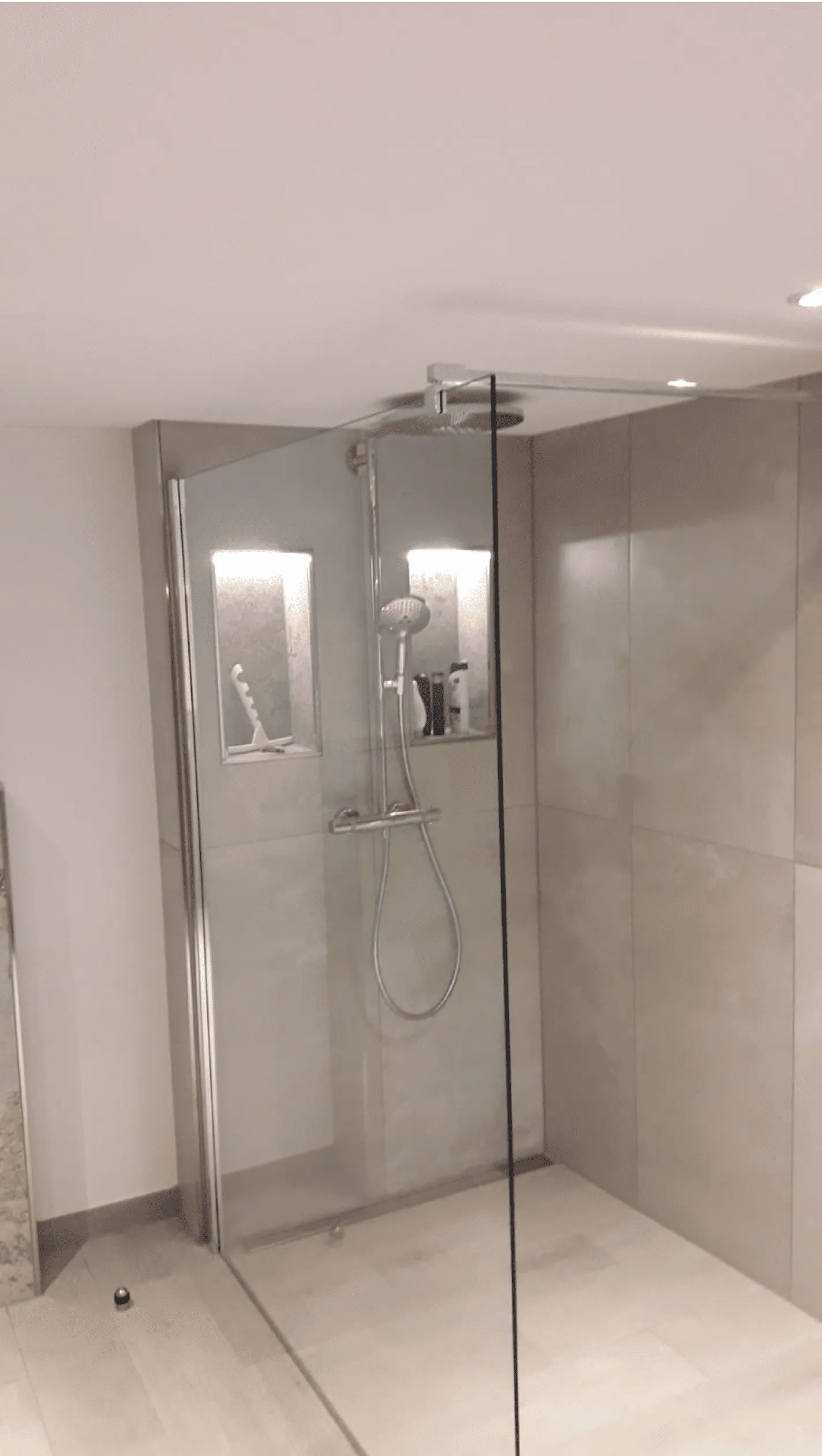 Moderne begehbare Dusche mit Glaswand, Regendusche und eingebauten Ablagen mit Shampoo und Duschgel.