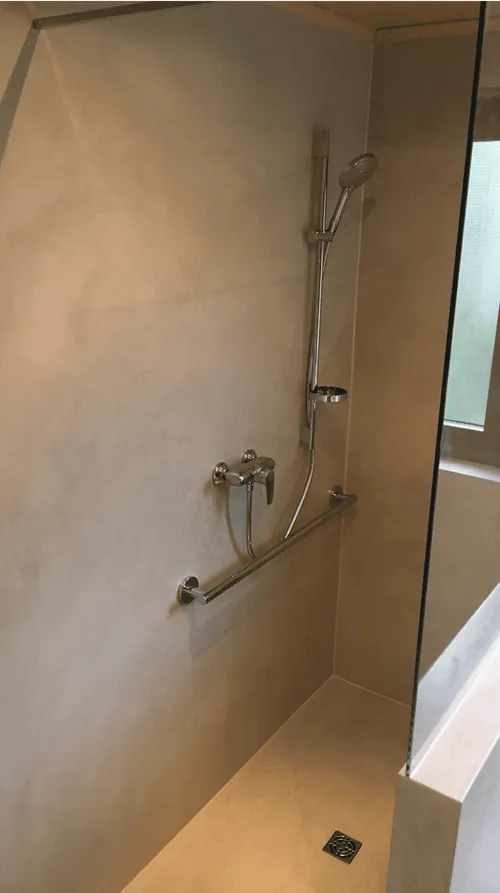 Minimalist shower area with beige walls, a wall-mounted handheld showerhead, metal faucet, grab bar, and a floor drain.