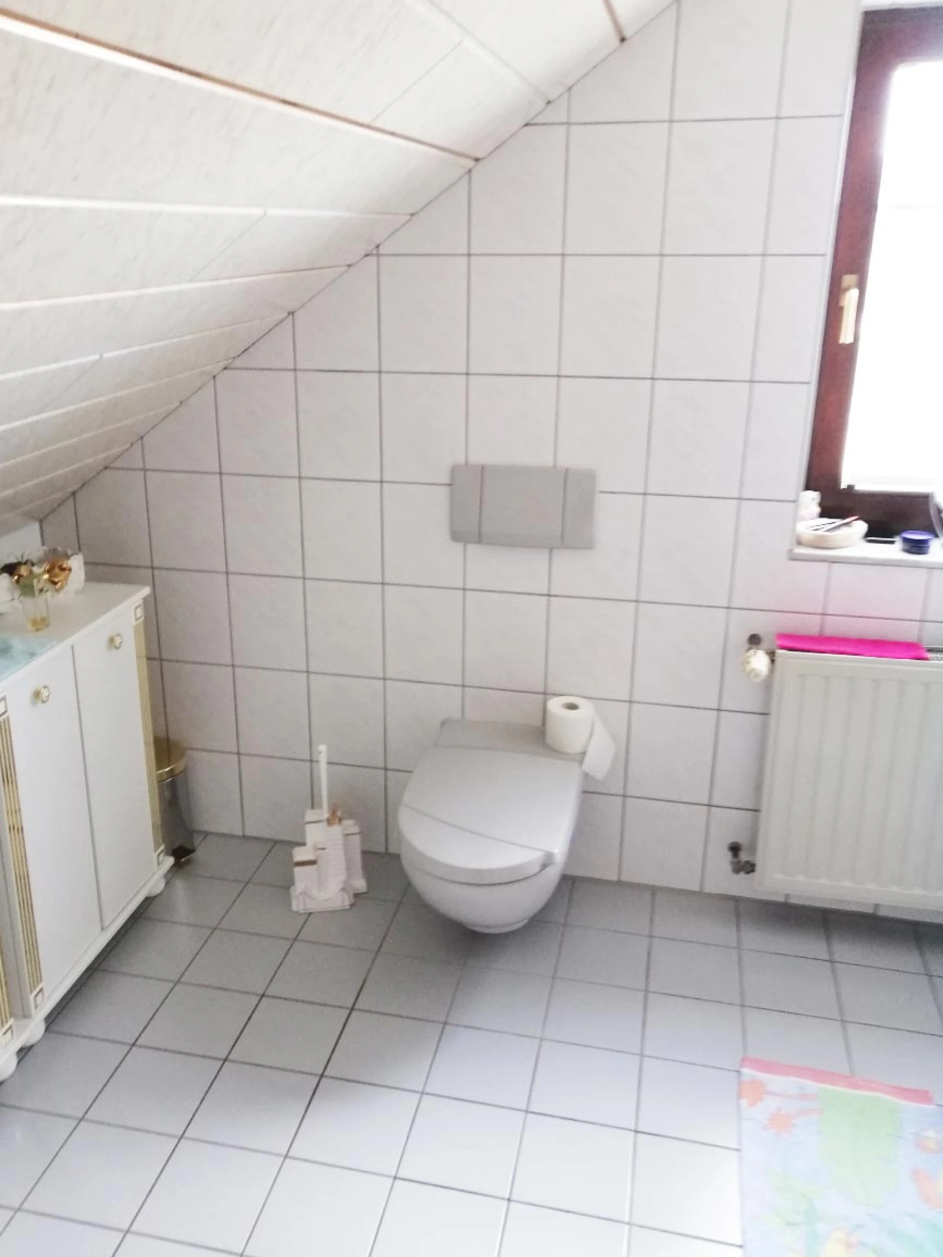 Modernes Badezimmer mit wandhängendem WC, Toilettenpapier, weißem Fliesenspiegel und Fenster.
