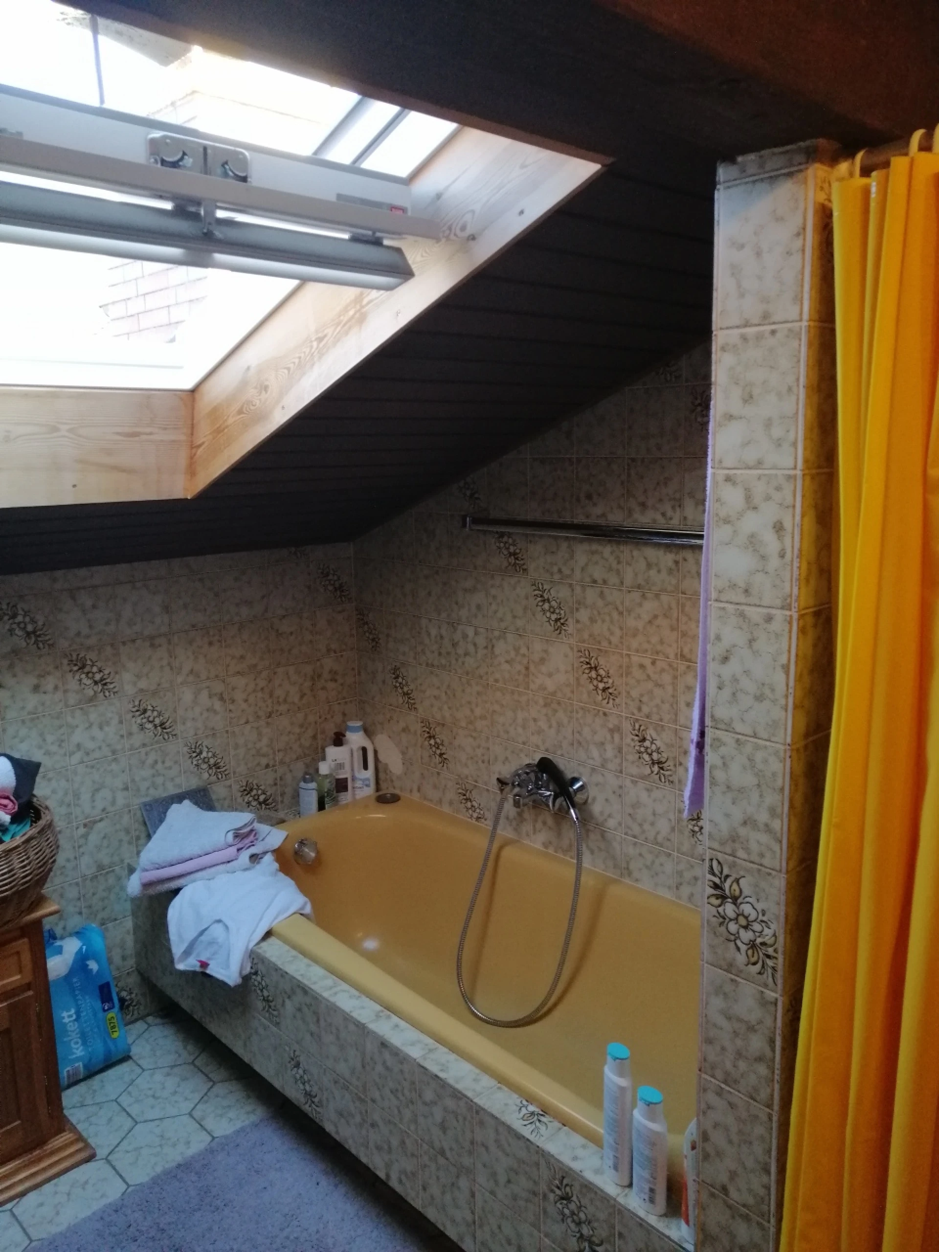 Badezimmer mit gelber Badewanne, gefliesten Wänden und Dachfenster, ein gelber Duschvorhang rechts.