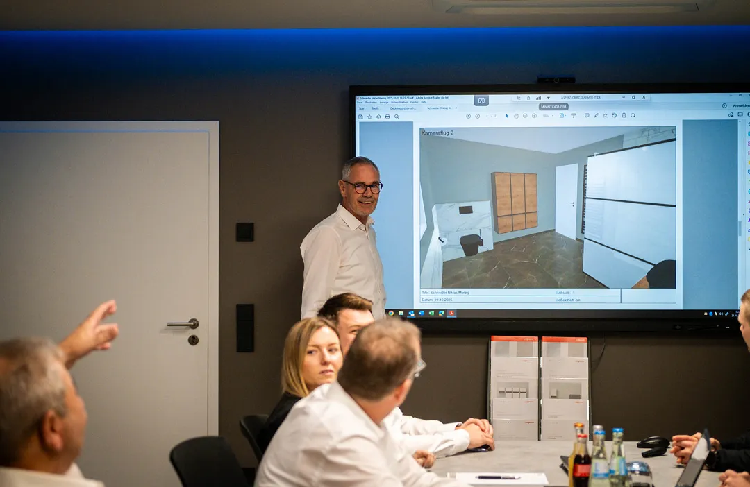 Ein Mann präsentiert eine Raumplanung auf einem Bildschirm vor einer Gruppe von Personen in einem Konferenzraum.