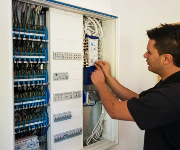 Elektriker arbeitet an einem geöffneten Sicherungskasten mit vielen Kabeln und Schalttafeln.