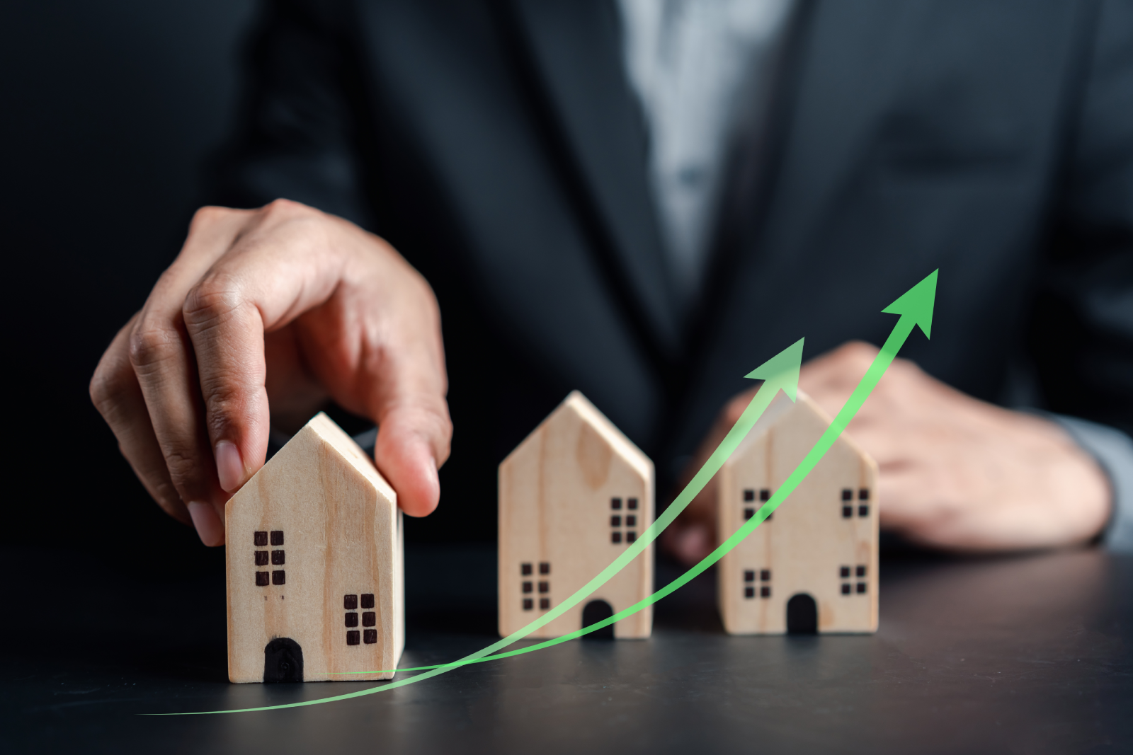 Hand arranging wooden house models along a rising green growth arrow