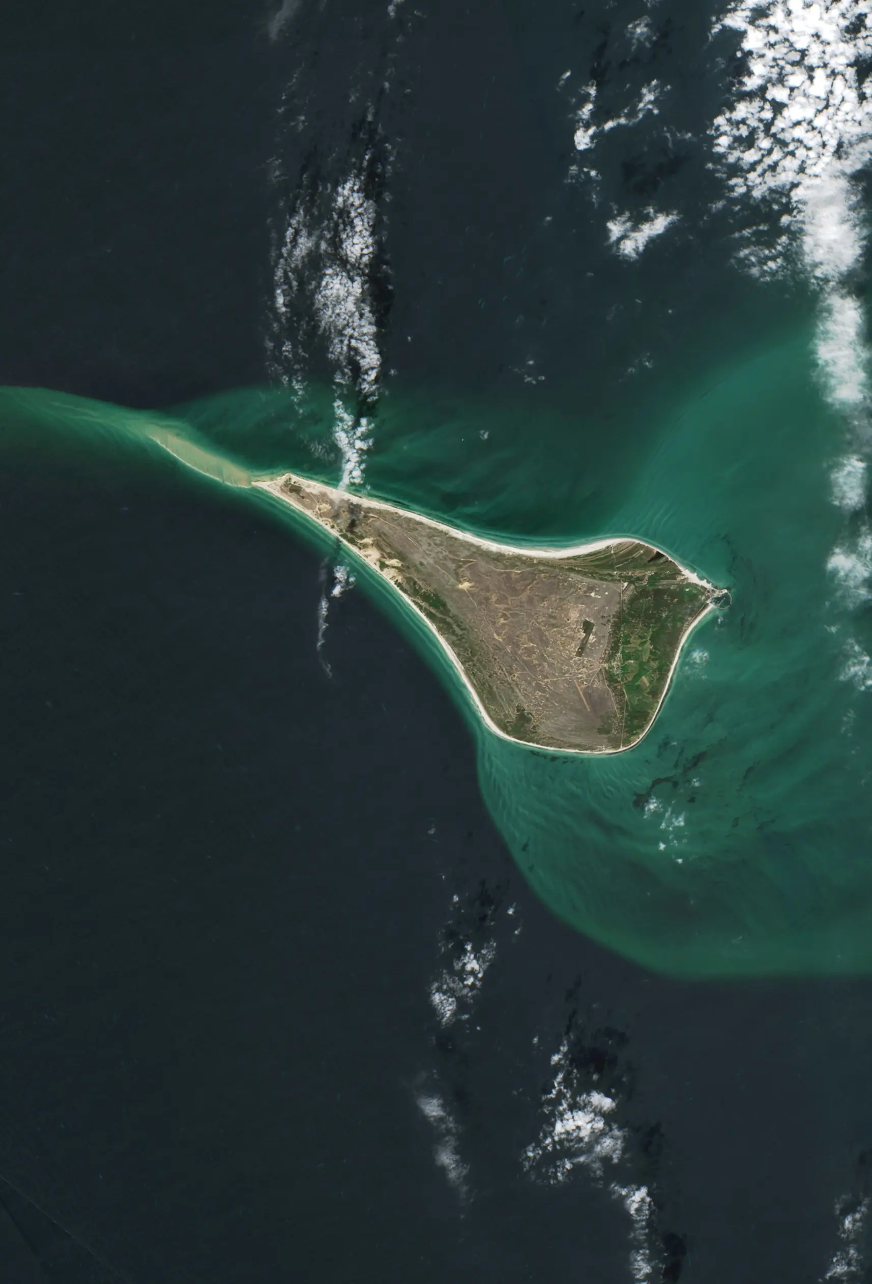 Aerial satellite view of a triangular island surrounded by dark ocean water with lighter turquoise shallow areas near its shores.