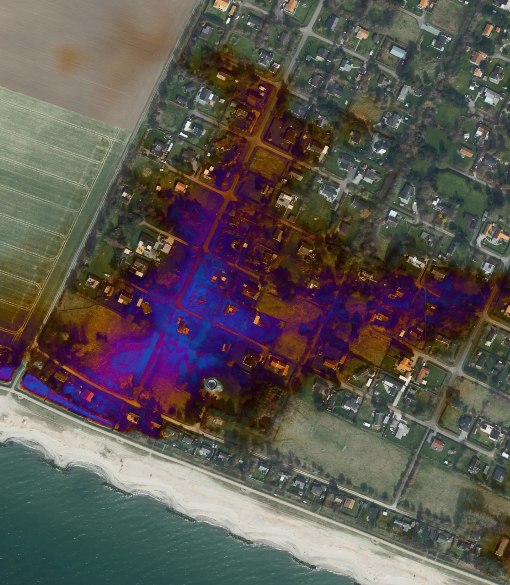 Aerial view of a coastal residential area with patches of digital overlay showing blue and orange heatmap-like patterns over streets and houses near the beach.
