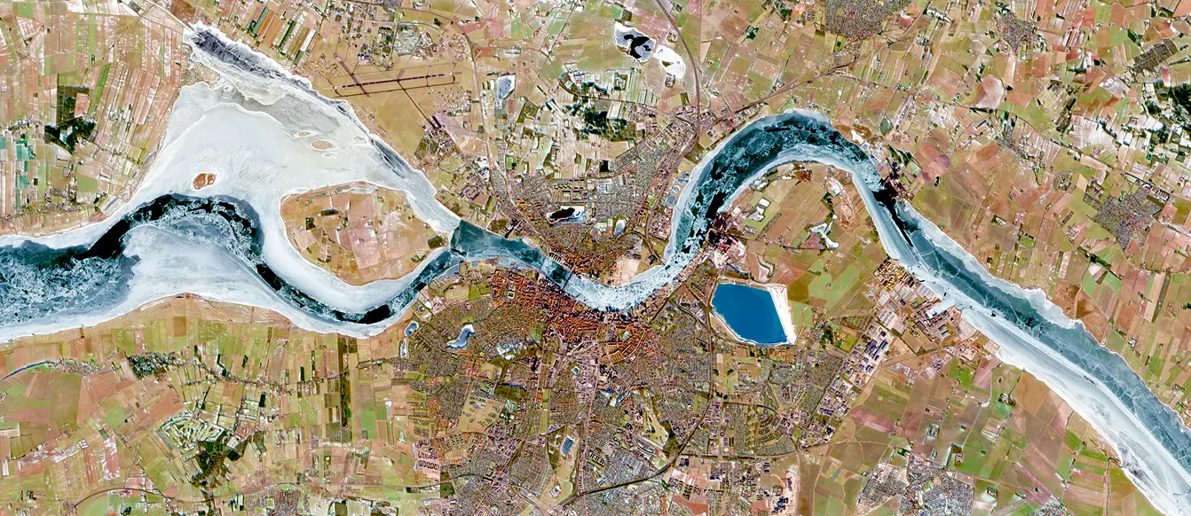 Aerial view of a city with a winding frozen river running through farmland and urban areas.