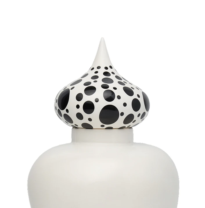White ceramic jar with a lid topped by a pointed, bulbous finial decorated with black polka dots.