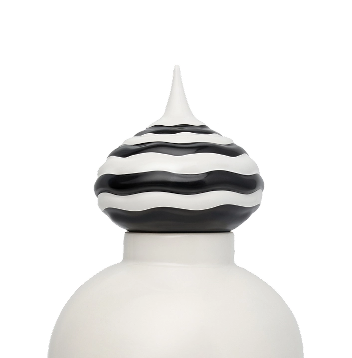 Close-up of a white ceramic jar lid with a pointed top and wavy black and white striped pattern.