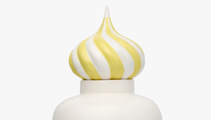 Close-up of a white ceramic container with a yellow and white striped swirl-shaped lid.
