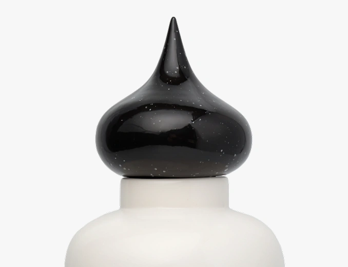 Close-up of a black, glossy, speckled ceramic finial atop a white round base.