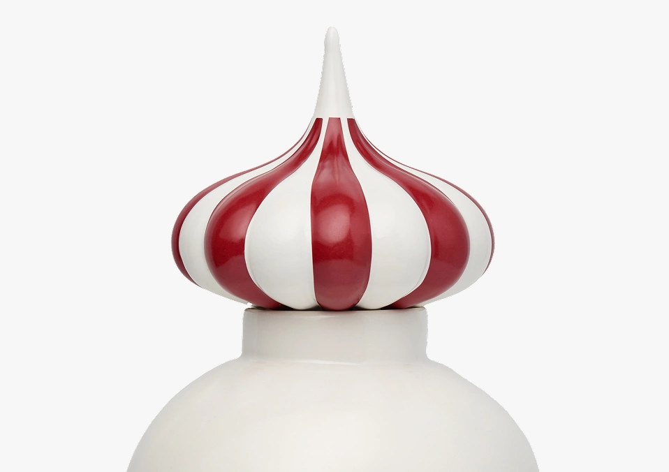 Close-up of a decorative ceramic lid with red and white striped pointed finial on a white round container.