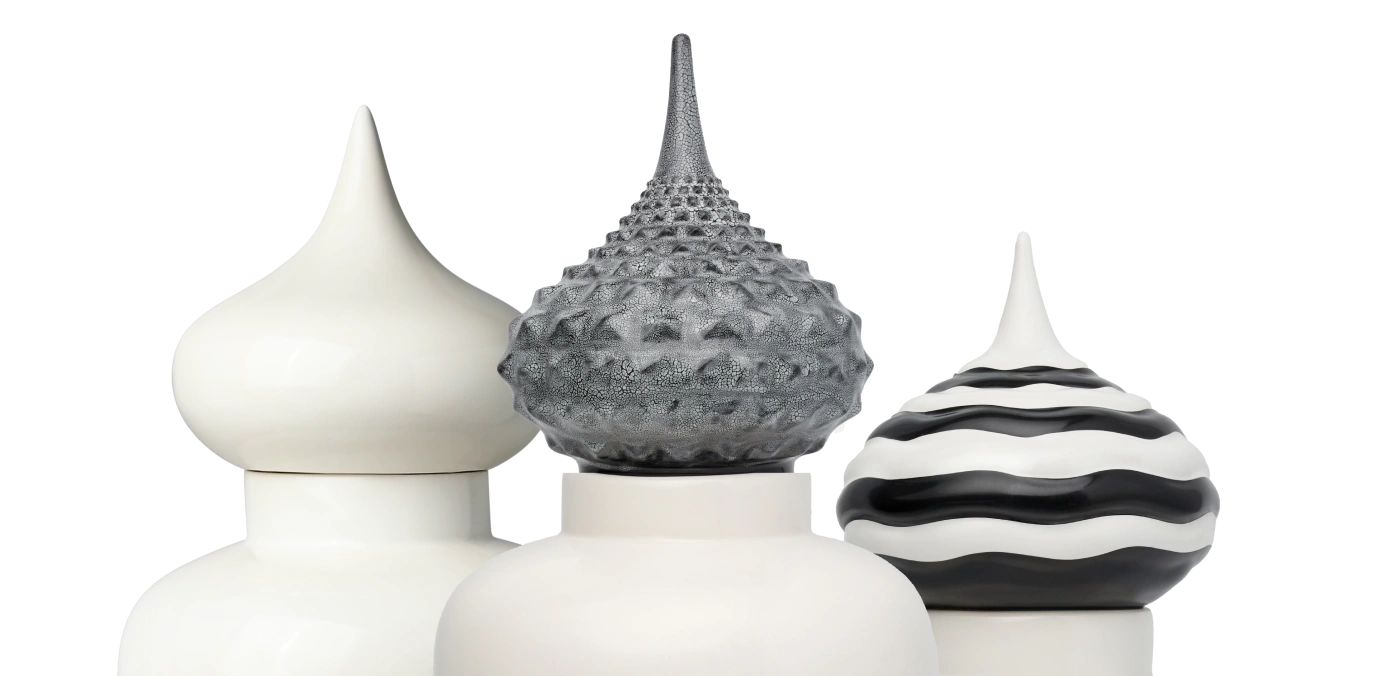Close-up of three decorative ceramic jars with pointed lids, featuring smooth white, textured gray, and black-and-white striped designs.