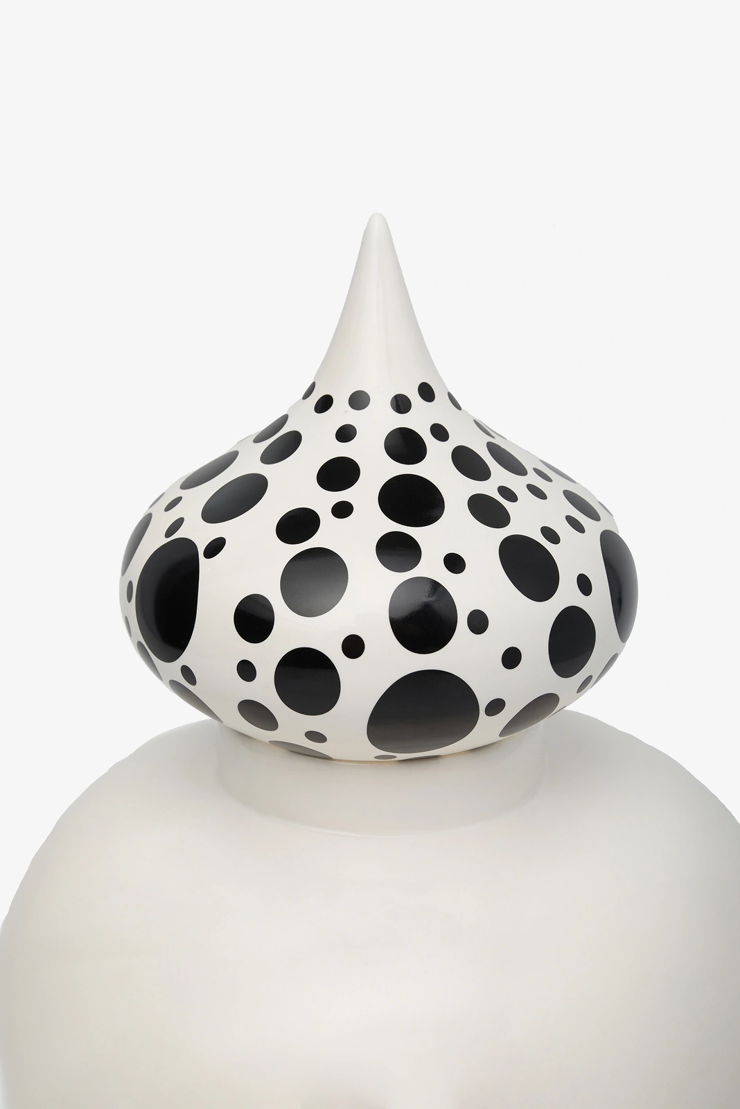 White sculptural form with a pointed top decorated with varying sizes of black polka dots.
