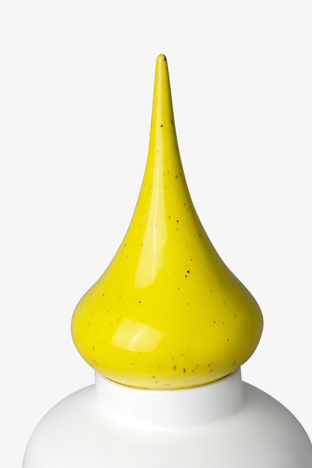 Close-up of a white container topped with a pointed yellow cap with dark speckles.