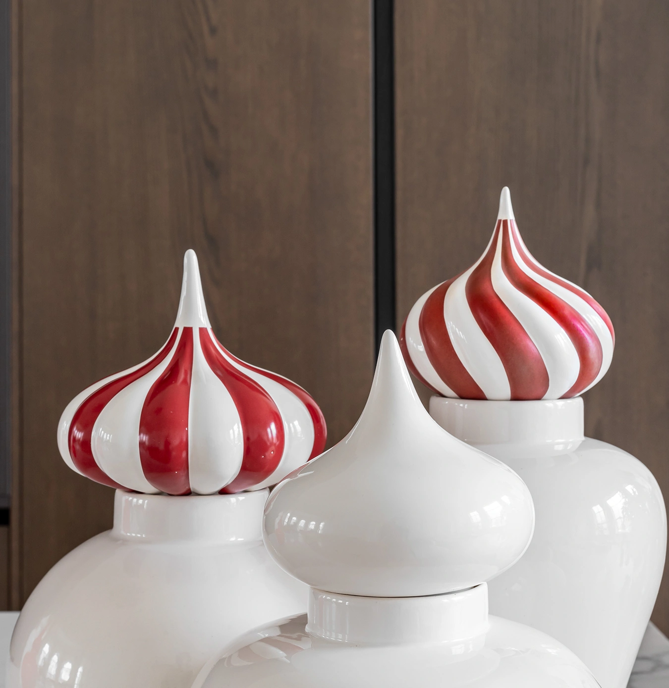 Three white ceramic jars with pointed lids, two featuring red and white stripes, against a brown wooden background.