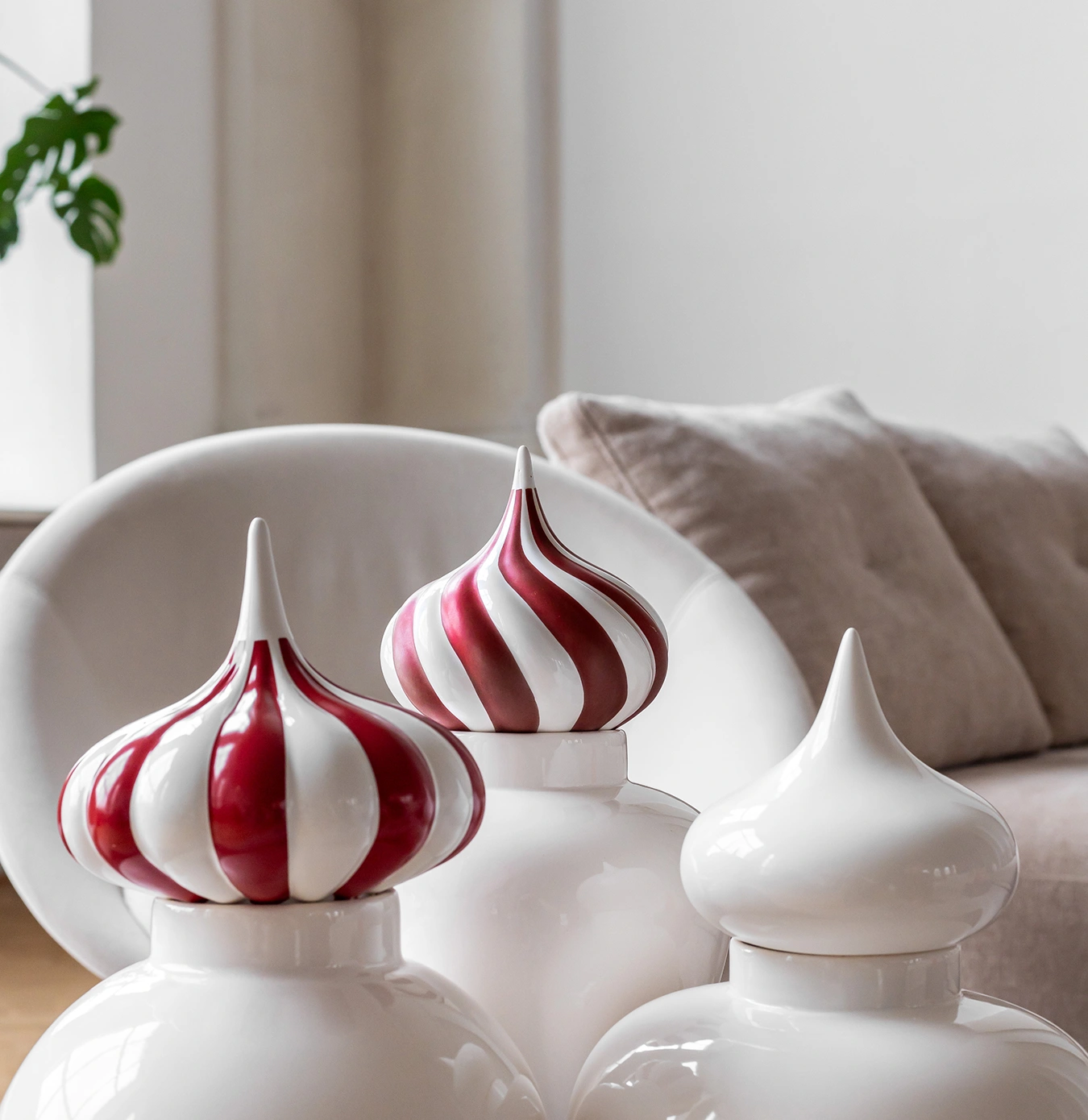 Three white decorative ceramic jars with pointed lids, two with red and white stripes, placed in a modern living room setting.