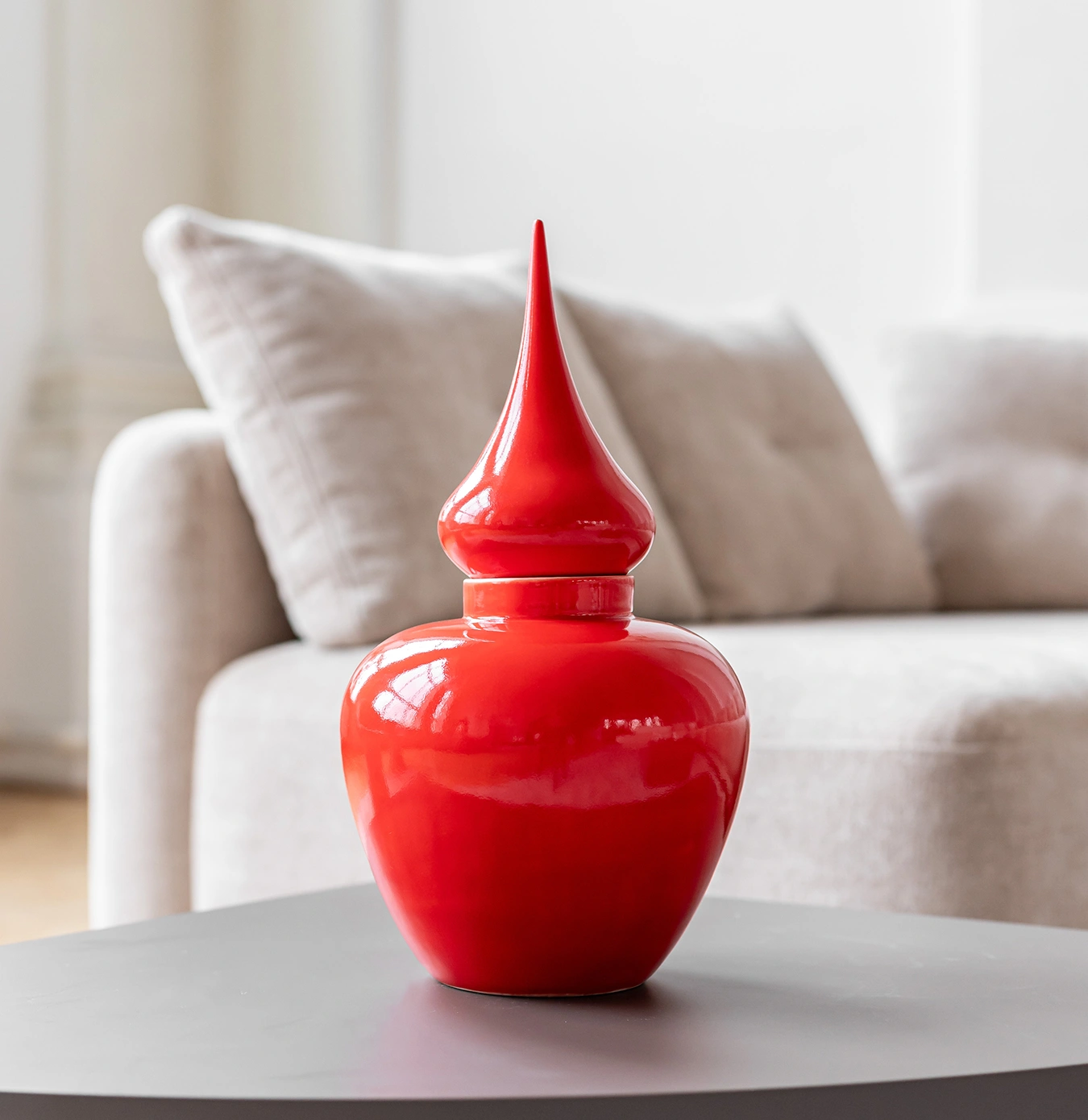 Glossy red decorative jar with a pointed lid on a black table in a living room.