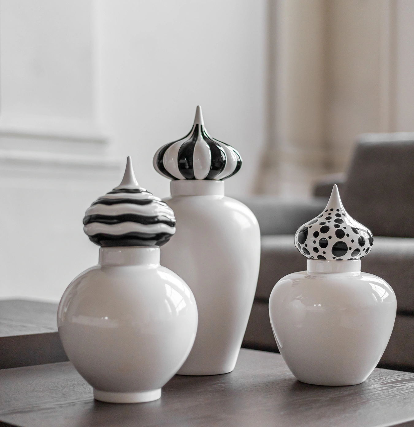 Three white ceramic jars with pointed black-and-white patterned lids displayed on a wooden surface in a living room.