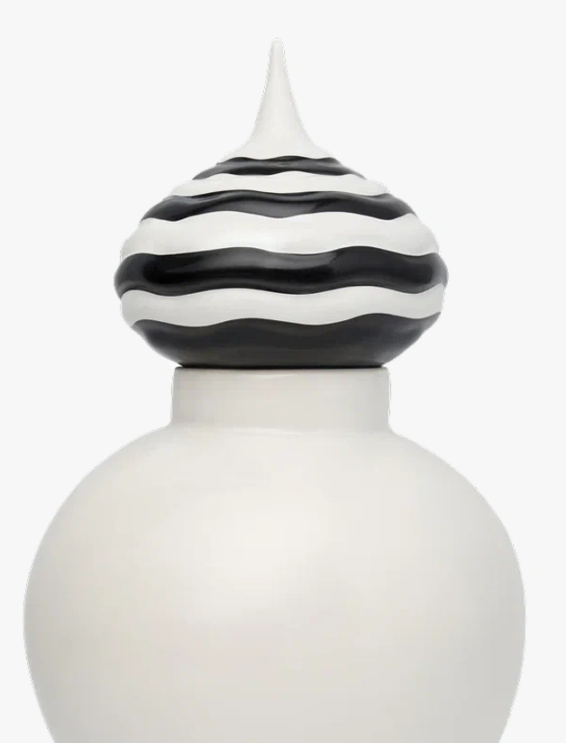 Close-up of a white vase with a black and white striped pointed lid with wavy patterns.