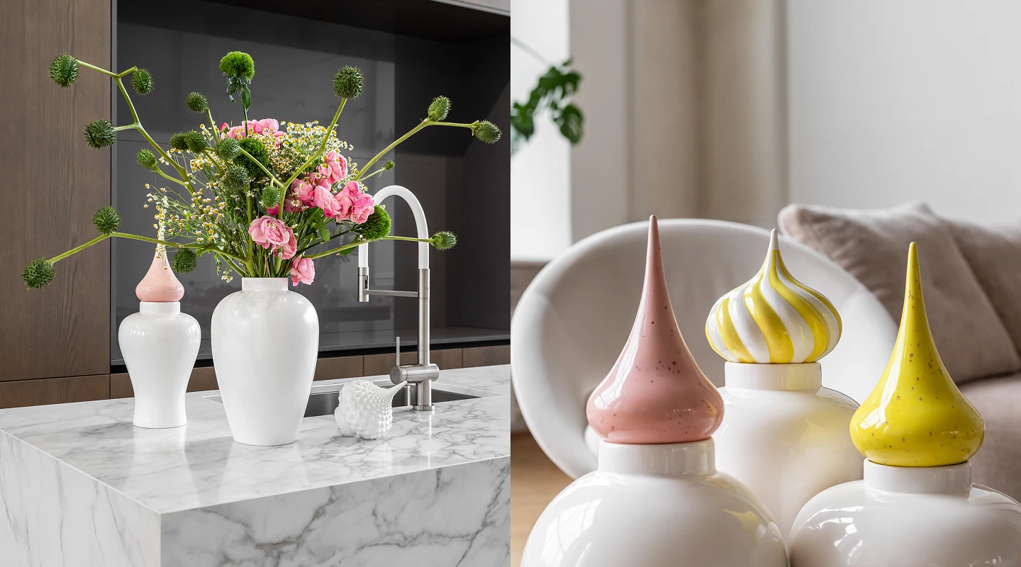 Modern kitchen island with marble countertop holding white vases, one with pink and green floral arrangement and others with decorative pointed lids in pink and yellow.
