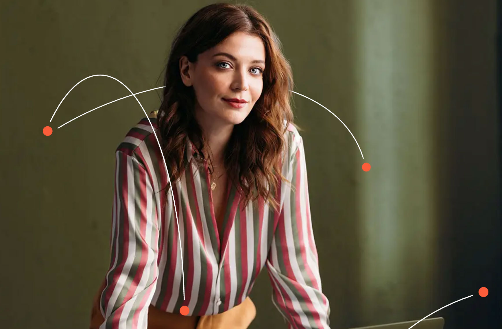 Young woman with wavy brown hair wearing a striped shirt leaning forward and smiling slightly.