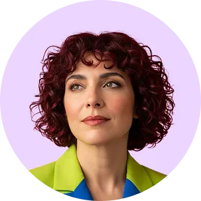 Portrait d'une femme aux cheveux bouclés courts rouges, portant une veste verte et bleue, sur un fond lilas.