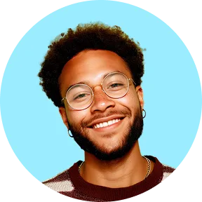 Portrait d'un homme souriant avec des lunettes rondes, un bouc et des boucles d'oreilles, devant un fond bleu clair.