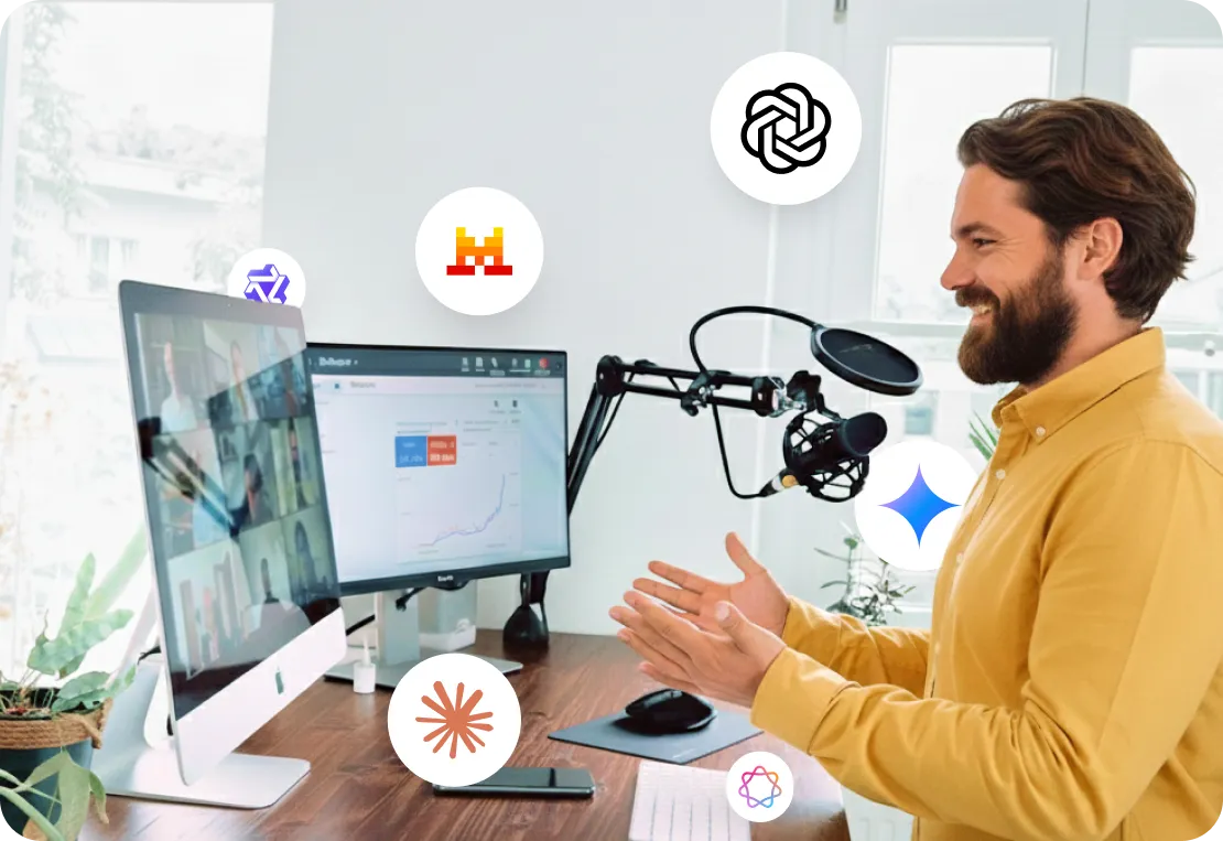 Un homme souriant en chemise jaune participe à une visioconférence devant deux écrans avec un microphone de studio sur un bureau moderne.