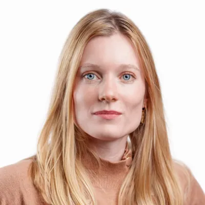 Portrait d'une femme blonde aux yeux bleus portant un pull marron clair, regardant directement la caméra.