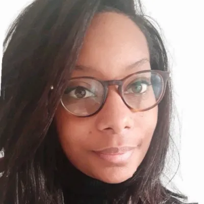 Portrait d'une femme portant des lunettes à monture marron et un pull noir, avec de longs cheveux noirs.