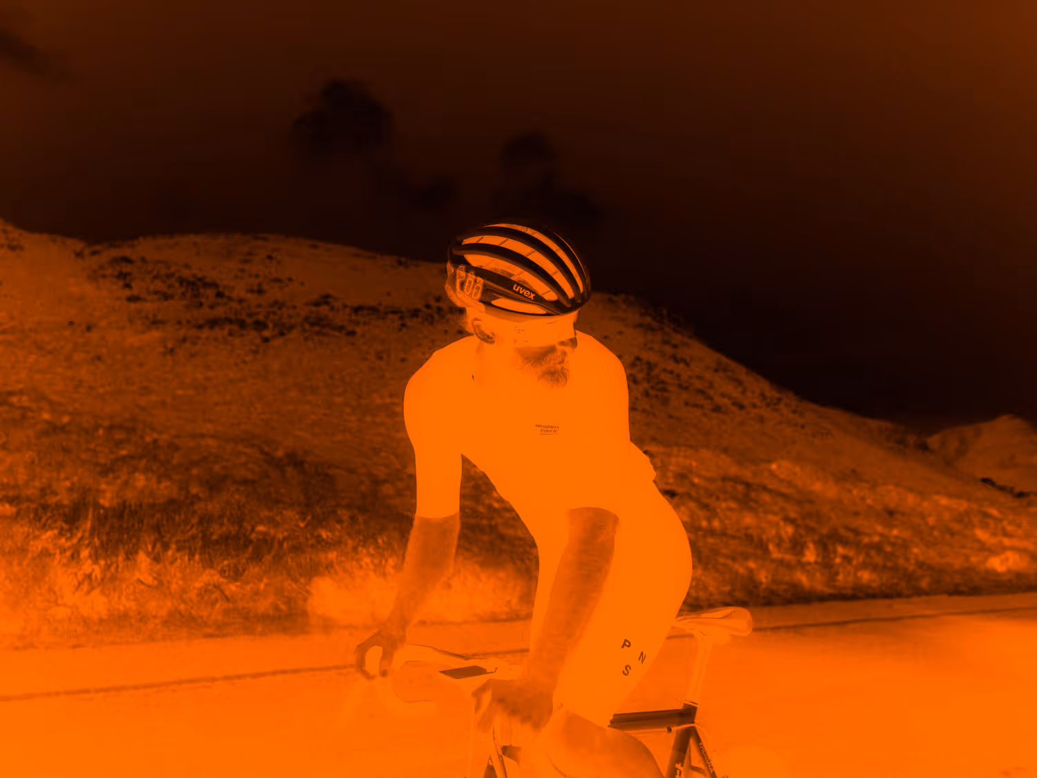 Man on a bike riding through hills with orange filter 