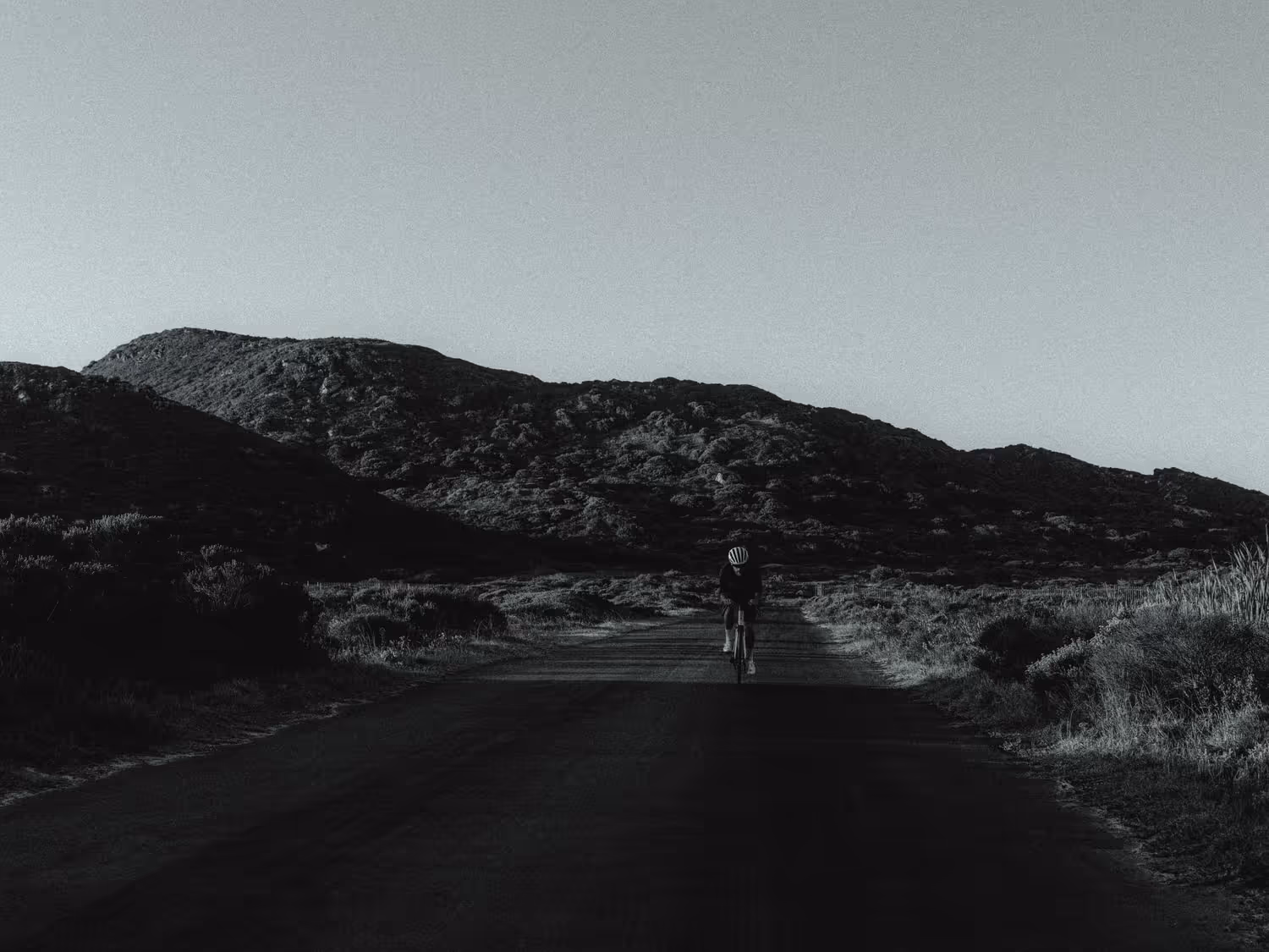 Black and white image of a man cycling down the road on a bike