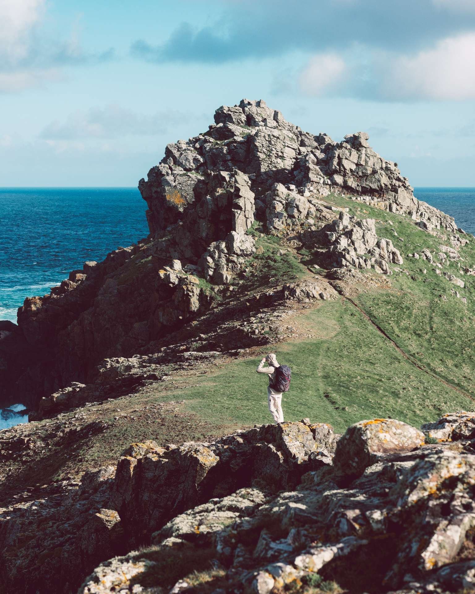 person stood on rocky hill by sea