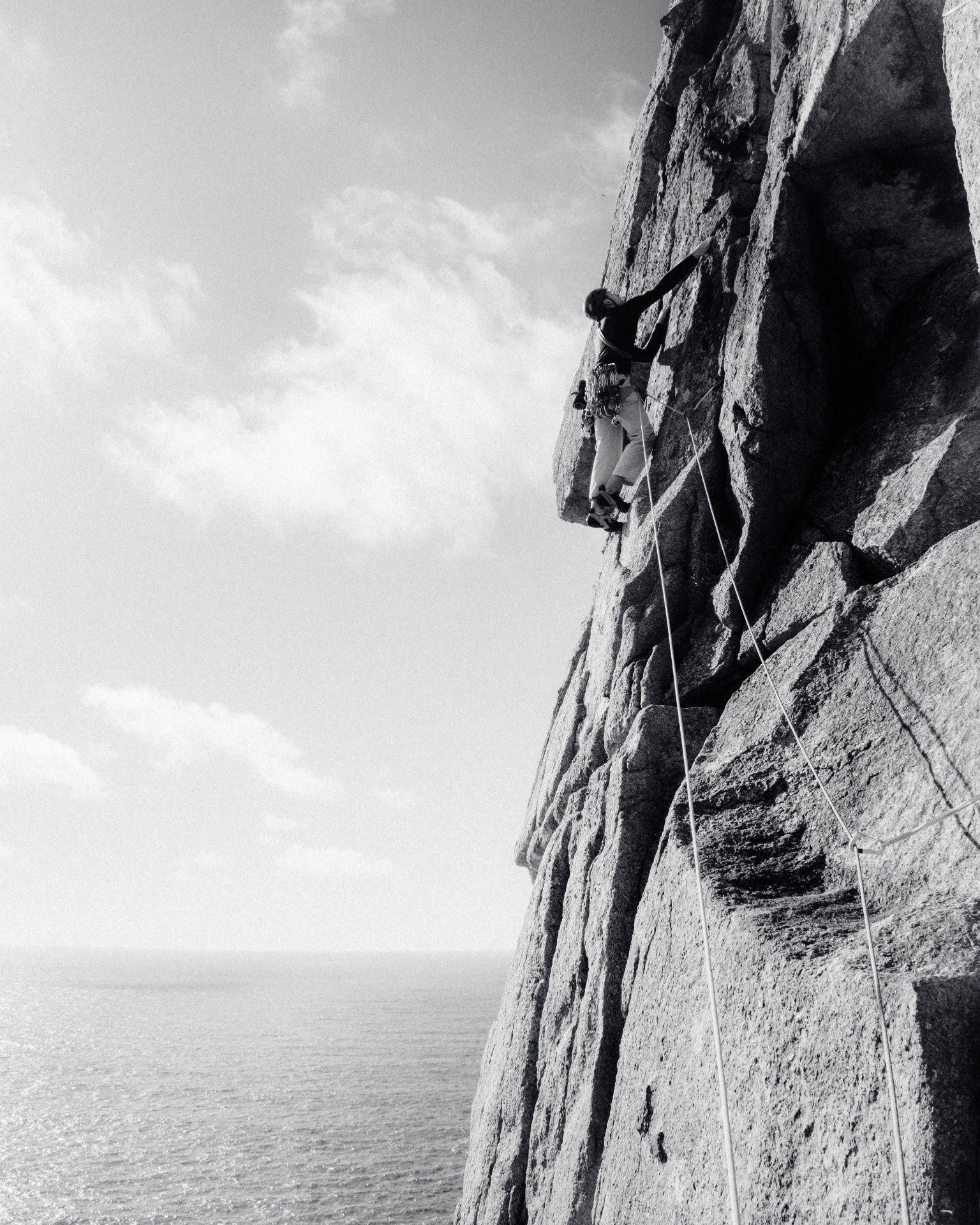 Black and white image of man climbing on cliff side 