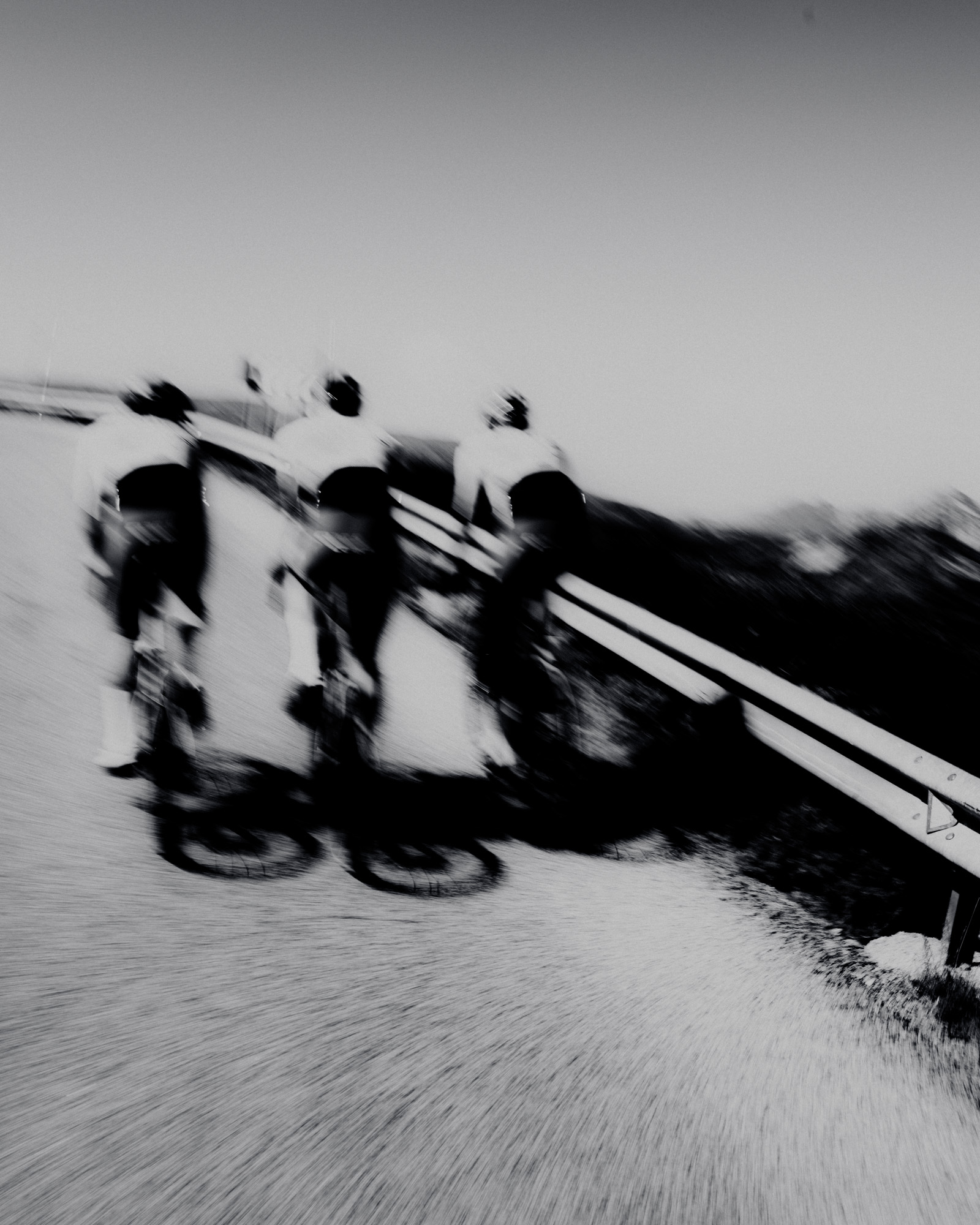 Blurred black and white image of three men cycling 